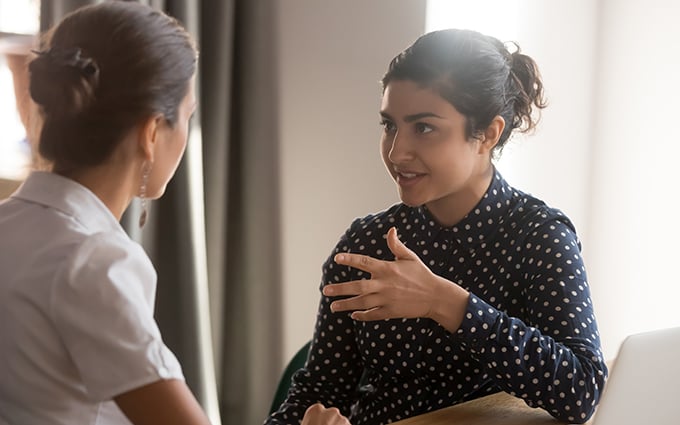 Two female colleagues having a conversation sitting at a desk