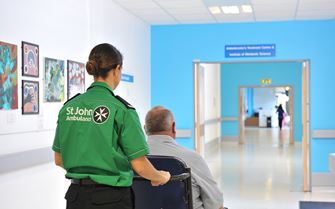 Ambulance staff pushing patient in wheelchair down a hospital corridor. 